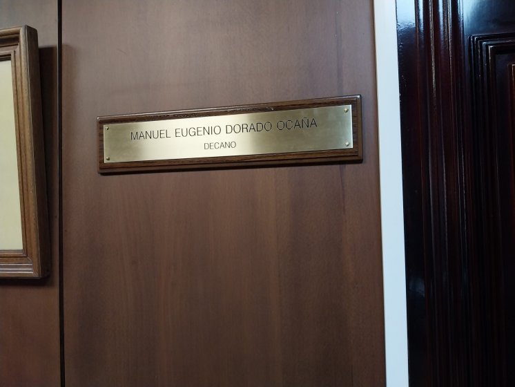 Rotulo en lat&oacute;n grabado en bajo relieve y patina de tinta negra, sobre metopa o peana de madera. Facultad de Medicina de la Universidad de Sevilla.