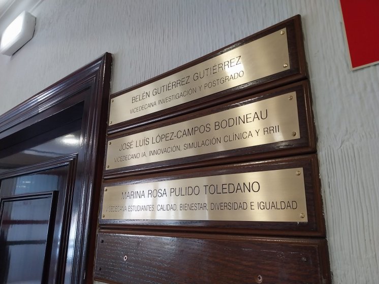 Rotulo en lat&oacute;n grabado en bajo relieve y patina de tinta negra, sobre metopa o peana de madera. Facultad de Medicina de la Universidad de Sevilla.