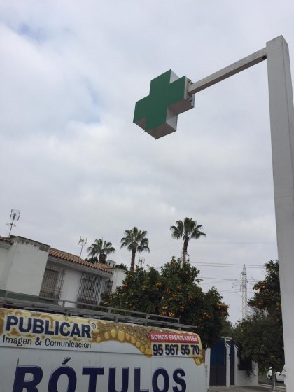 Rótulo cruz de farmacia y mástil montado sobre acerado en Sevilla.
