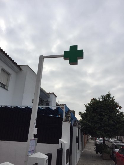 R&oacute;tulo cruz de farmacia y m&aacute;stil montado sobre acerado en Sevilla.